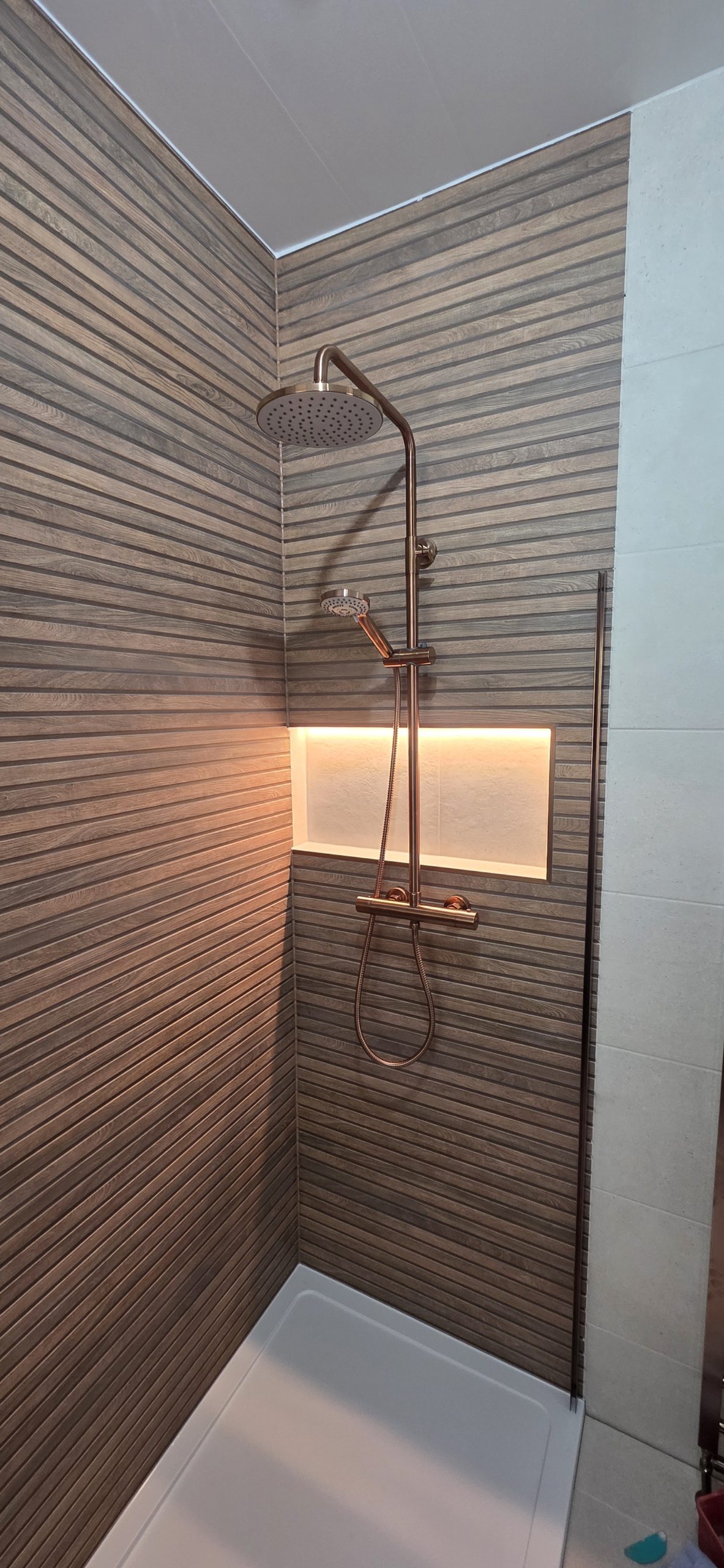 Shower with wood-effect feature wall and lit niche by Clan Bathrooms