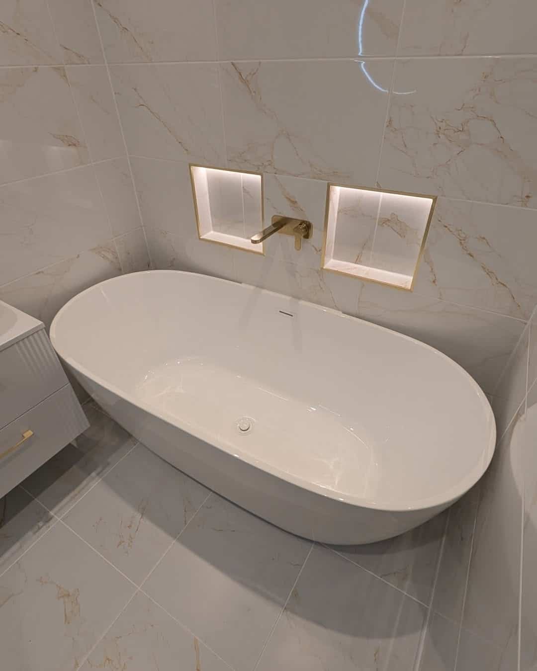 Oval freestanding bath with wall-mounted brushed brass tap and two LED-lit niches in a Dumbarton bathroom