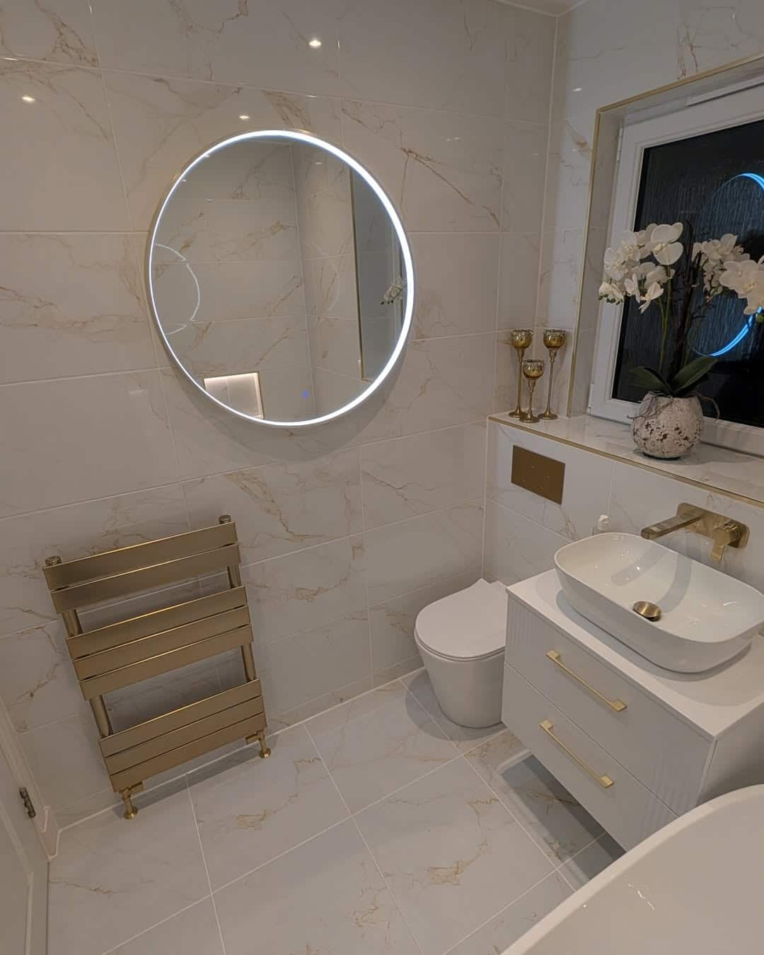 Brushed brass towel rail and round LED mirror in a marble-effect tiled bathroom in Dumbarton